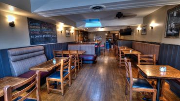 Cozy pub interior with wooden tables, chairs, and a chalkboard menu on the wall.