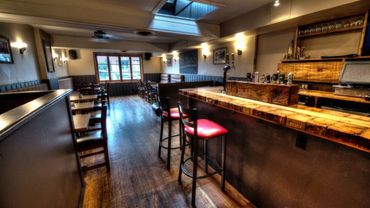 Cozy wooden bar interior with red cushioned stools and natural light from a skylight.