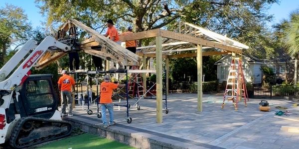 Construction workers building a wooden structure on a tiled patio next to a green putting area.