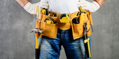 handyman with hands on waist and tool belt with construction tools against grey background. 