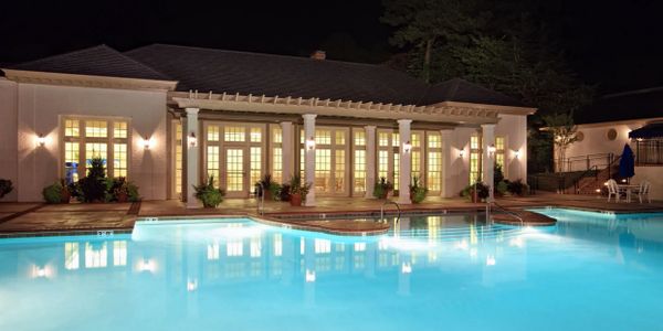 Elegant building with bright lights reflecting in a calm swimming pool at night.
