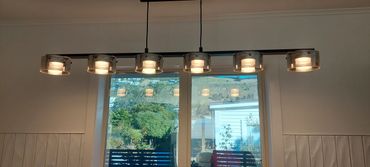 Modern ceiling light fixture with six cylindrical glass shades above a window.