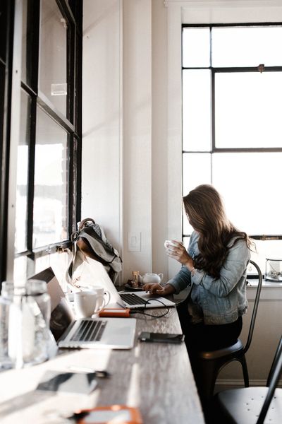 woman holding coffee while on laptop in office