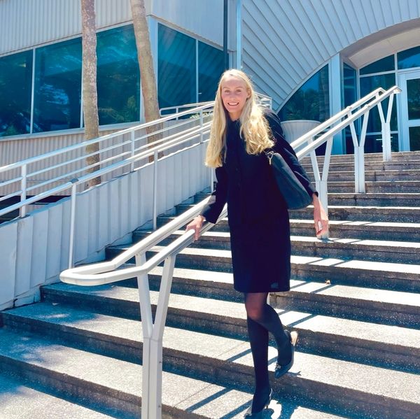 Smiling woman in black dress on stairs outside a modern building.