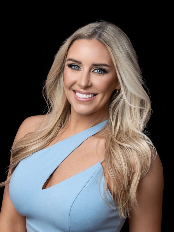 Smiling blonde woman with blue eyes in a light blue dress.
