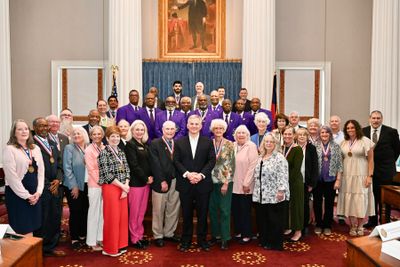 A diverse group of people posing for a formal group photo in a decorated room.