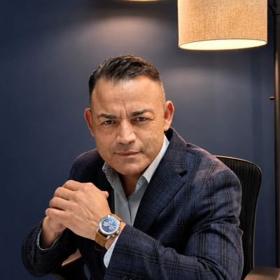 Man in a suit sitting confidently with a watch in a dimly lit room.