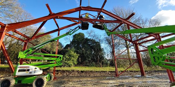 Two steel erectors fitting a structural steel frame from cherry pickers.