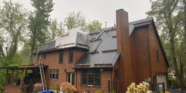A brown house with a new roof under construction surrounded by trees.