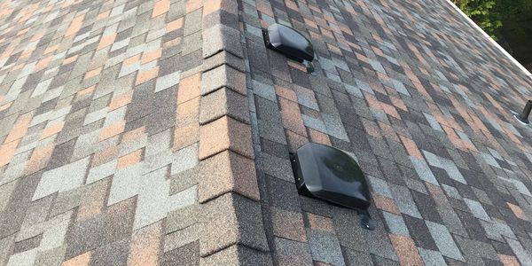 A rooftop with multicolored shingles and two black vents.