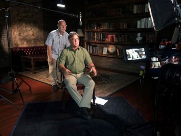 Bradley Williamson being filmed with the Sound Tech behind him checking on microphone.