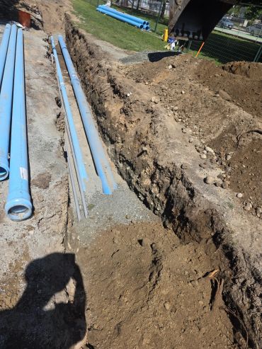 Construction site with blue pipes being installed in a trench.