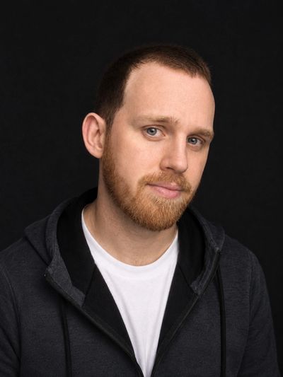 Man with beard and hoodie against black background.