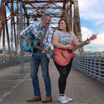man and woman holding guitars on a bridge