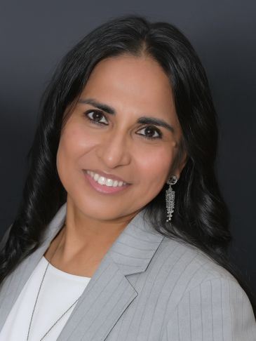 Smiling woman in a gray blazer against a dark background.