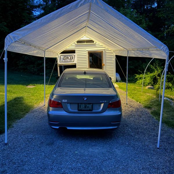 Silver BMW 3 Series parked under a white canopy in front of a small building.