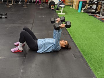 a woman is lying on the floor with a set of dumbbells extended over her body 