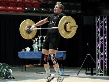 a female weightlifter is pulling the barbell using a snatch grip and is fully extended