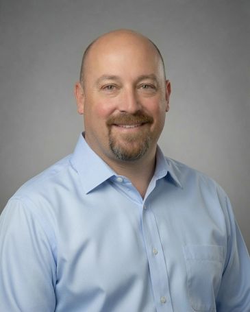 Smiling man in blue shirt against gray background.