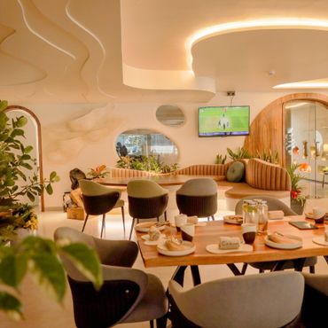 Modern dining area with curved ceiling, cozy seating, and lots of greenery.