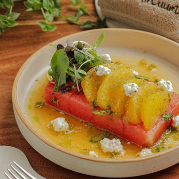 Fresh watermelon salad with orange slices, microgreens, and cheese on a wooden table.