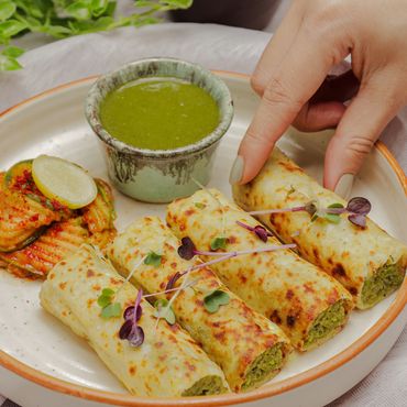 Hand picking a stuffed Indian roll served with green chutney and salad.