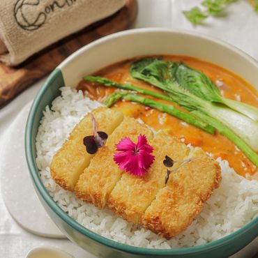 Crispy fried tofu with rice and curry, garnished with fresh greens and edible flowers.