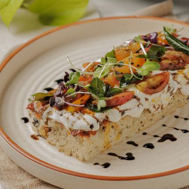 Gourmet bread topped with fresh tomatoes, greens, and creamy spread with balsamic drizzle.