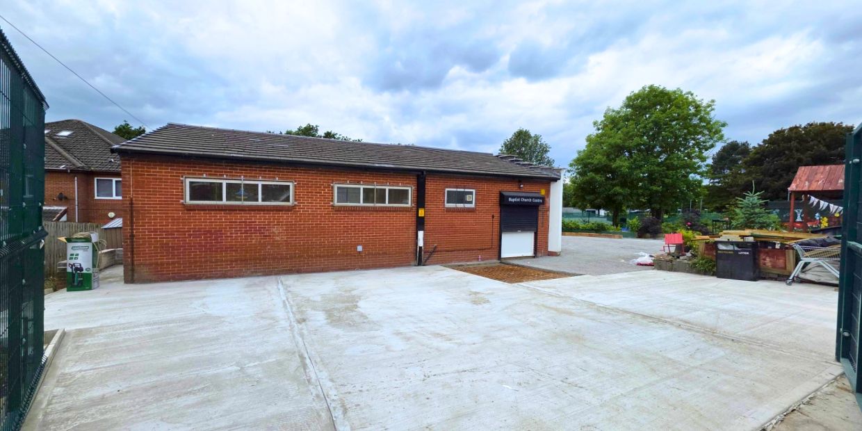 Brick Baptist Church Centre with concrete surroundings and cloudy sky.
