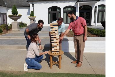 Four people playing giant Jenga outdoors on a sunny day.