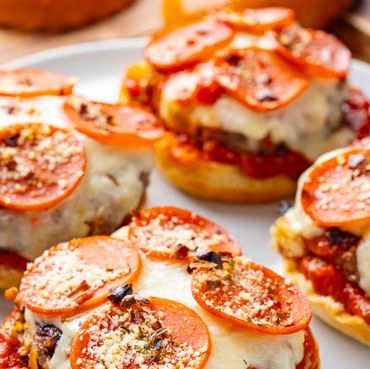 Mini cheeseburger pizzas topped with pepperoni and herbs on a plate.