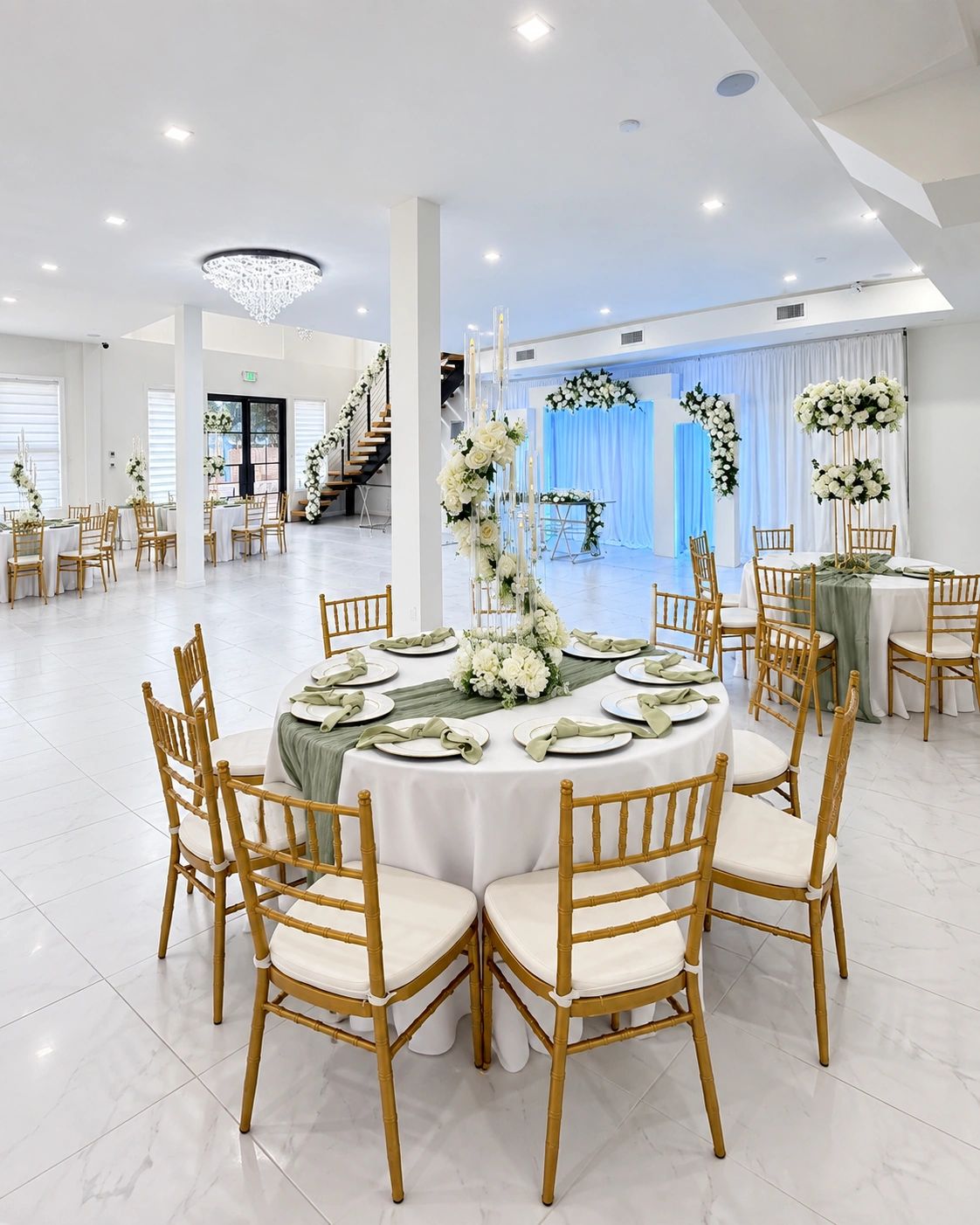 Spring Gatherings event venue with white tables, gold Chiavari chairs, floral décor, a chandelier, a