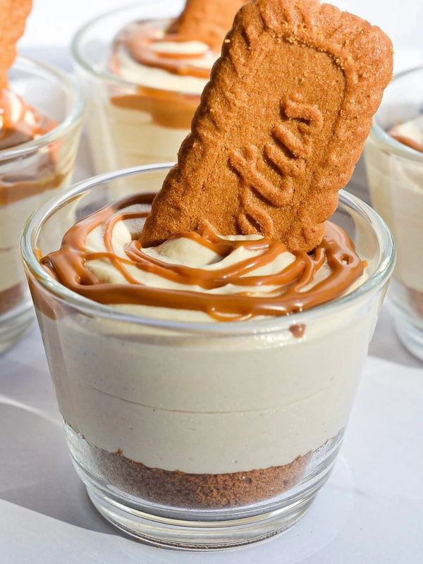 Glass of creamy dessert topped with caramel drizzle and a Lotus biscuit.