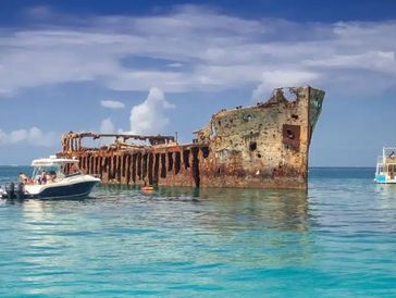 Rusty shipwreck in clear blue water with boats nearby.