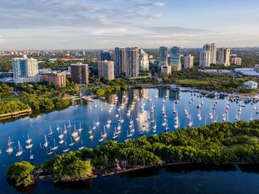 Aerial view of a marina with sailboats and city skyline in the background.
