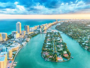 Aerial view of a coastal city with waterways and high-rise buildings at sunset.