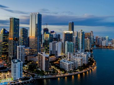 Evening skyline of a modern city with illuminated skyscrapers by the water.