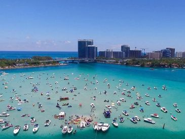 Numerous boats anchored in clear turquoise water near a coastal city skyline.