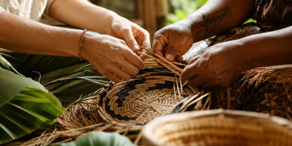 Two people weaving a basket together using natural fibers.