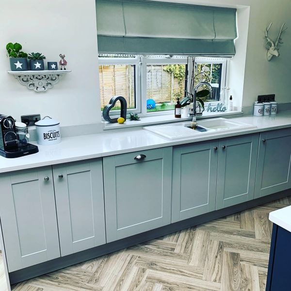 Modern kitchen with gray cabinets, white countertops, and wooden herringbone flooring.