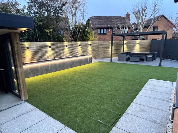 Modern backyard with artificial grass, ambient lighting, and outdoor seating area.