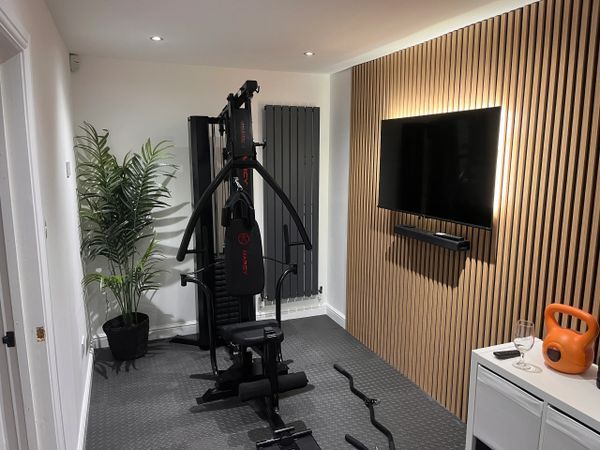 Modern home gym with exercise equipment, TV, and stylish wooden panel wall.