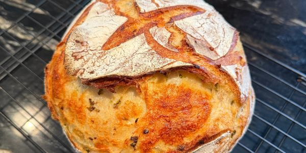 Crusty round loaf of bread with herbs on a cooling rack.