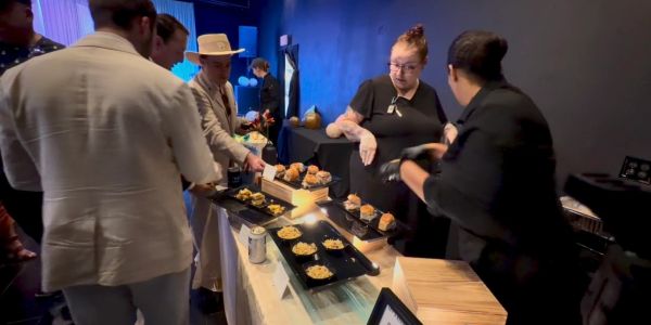 People serving and enjoying pastries at a food event.