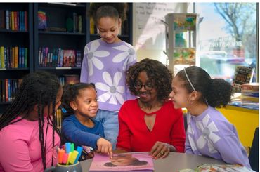 A group of children and an adult woman enjoy reading a book together in a library.