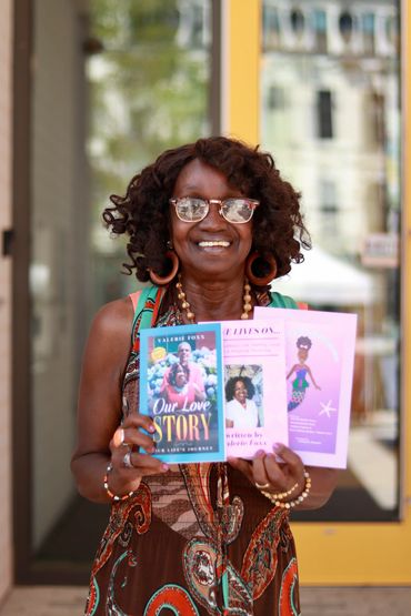 Smiling woman proudly holding three colorful booklets in front of a building.