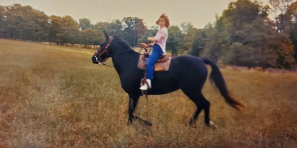 Jennifer Peachee-Harris as a young equestrian, riding through a field on her black mare, Glory.