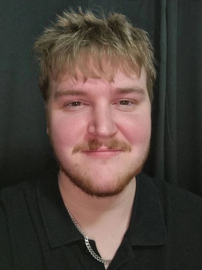 Young man with light brown hair and a trimmed beard smiling gently.