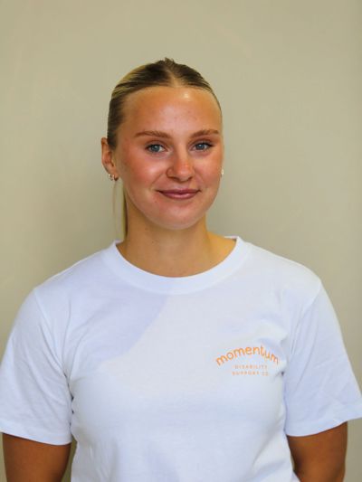 Smiling young woman in a white Momentum t-shirt against a plain background.