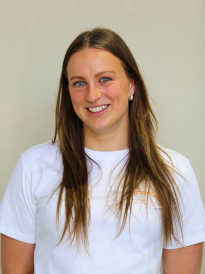 Smiling woman with long brown hair in a white t-shirt against a plain background.